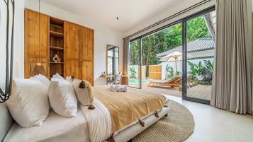 A bedroom with a large bed, wooden wardrobe, and a view of a pool area.