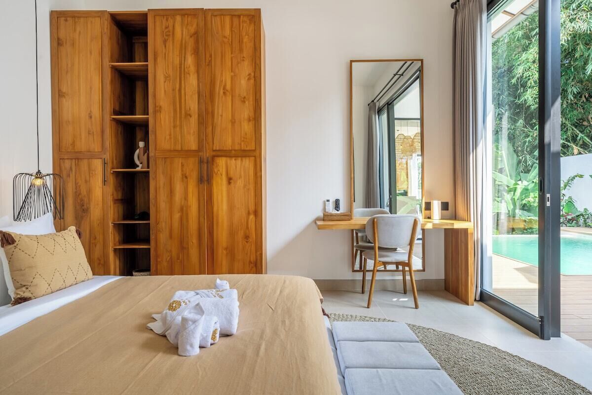 Un dormitorio con una cama grande, un armario de madera, un escritorio con una silla y vistas a una piscina.