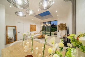 A modern interior with a dining area featuring a marble table, candles, and floral arrangements. - New 1BR Villa+Beach Access+Private Pool+South Kuta (Badung Regency)