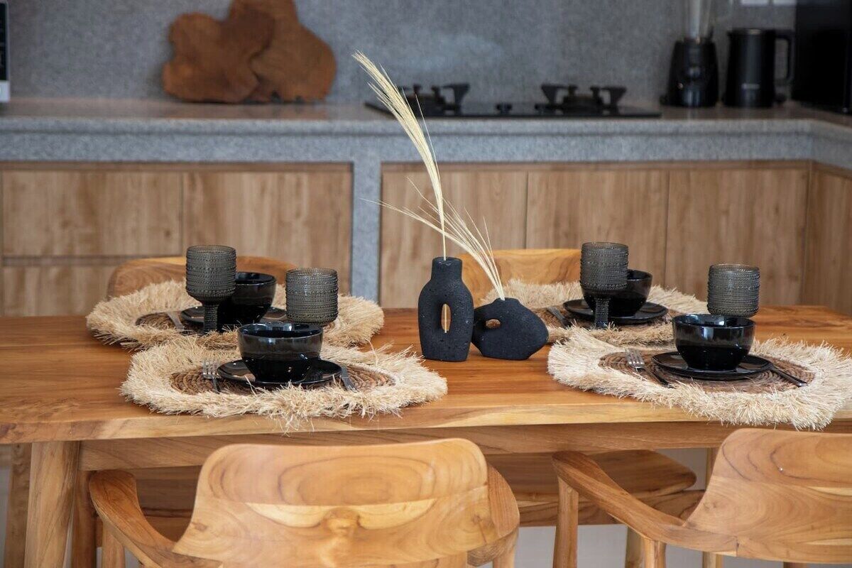 Ein Holztisch mit schwarzen Schüsseln und gewebten Tischsets, vor einer Wand aus Holzverkleidung und Stein.