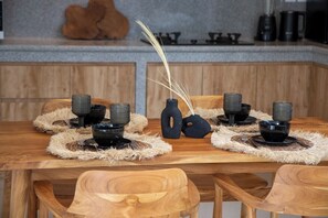 Ein Holztisch mit schwarzen Schüsseln und gewebten Tischsets, vor einer Wand aus Holzverkleidung und Stein.