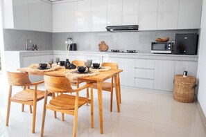 A modern kitchen with white cabinets, a granite countertop, a microwave, and a dining area with wooden chairs and a table. - Cozy 2BR Paradise w Beach Nearby & Huge Pool+Patio (Kabupaten Badung)