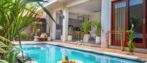 A modern outdoor pool area with a dining setup and potted plants.
