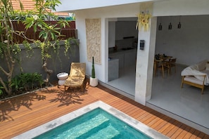 A pool area with a wooden deck, a lounge chair, and a dining area with a table and chairs. - Cozy 2BR Paradise w Beach Nearby & Huge Pool+Patio (Kabupaten Badung)