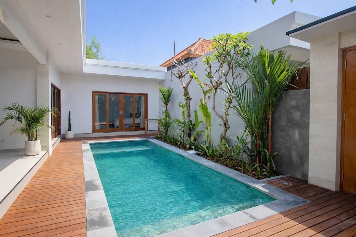 Ein moderner Poolbereich mit Holzterrasse, umgeben von Kübelpflanzen und einem Gebäude mit Glasfassade.