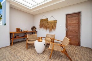 Ein Zimmer mit Holzboden, einem weißen runden Tisch, Korbstühlen, einer Holztür und einer an der Wand hängenden Uhr.