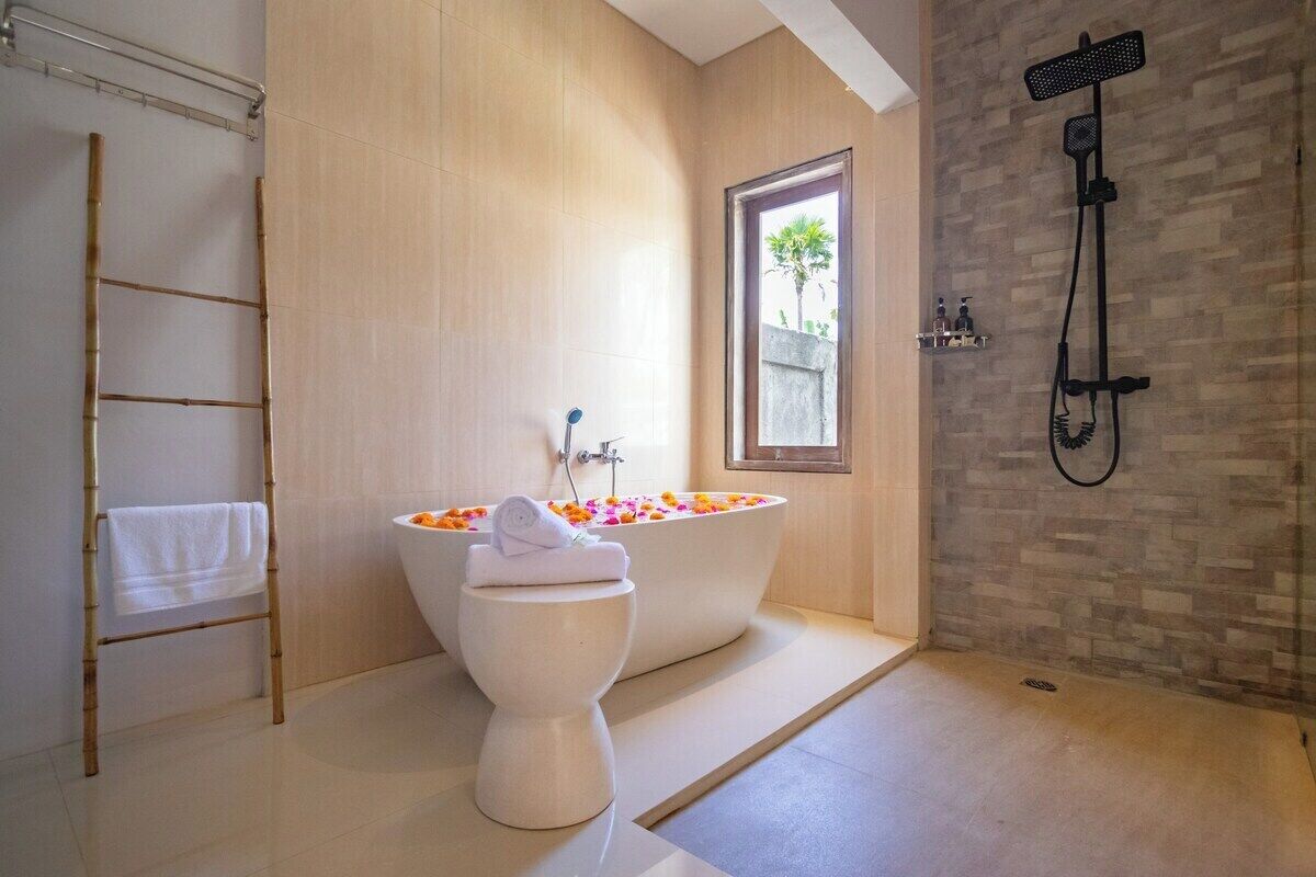 A bathroom with a freestanding bathtub filled with flower petals, a toilet, a shower area, and a window providing natural light.