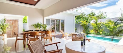 A modern interior with a dining area, a round table, and a view of a swimming pool and greenery.