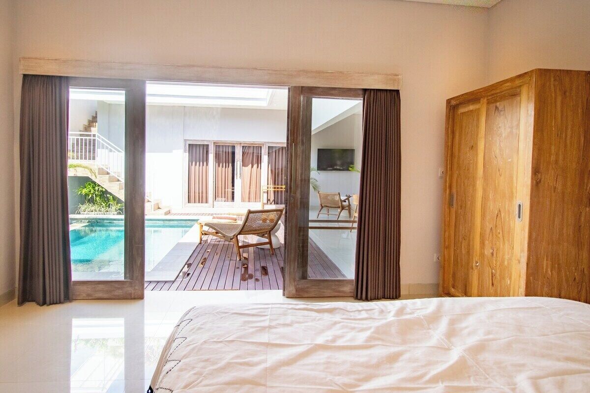 Een slaapkamer met een groot bed, een houten garderobe en uitzicht op een buitenzwembad.