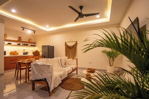 A modern living room with a sofa, a dining table, and chairs, a ceiling fan, and a kitchen area with cabinets and a refrigerator. - NEW Superb Villa, Beach access, Huge Private Pool (Badung Regency)