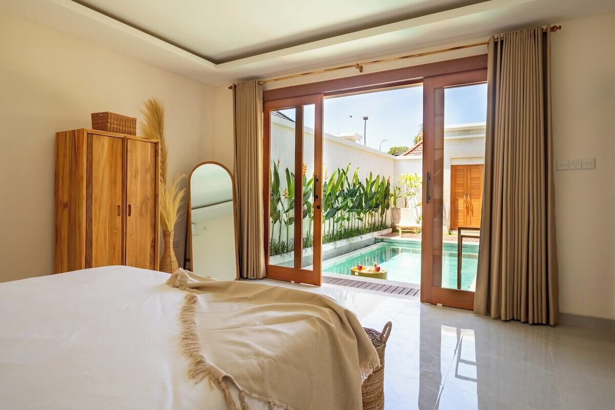 Un dormitorio con cama, un armario de madera, un espejo y una puerta corrediza de vidrio que da a una zona de piscina.