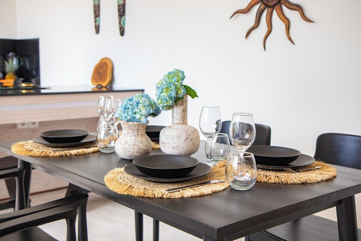 Una mesa de comedor dispuesta con platos, vasos y un florero con flores.