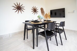 Un coin repas avec une table noire, quatre chaises, des éléments décoratifs muraux et un téléviseur à écran plat fixé au mur.