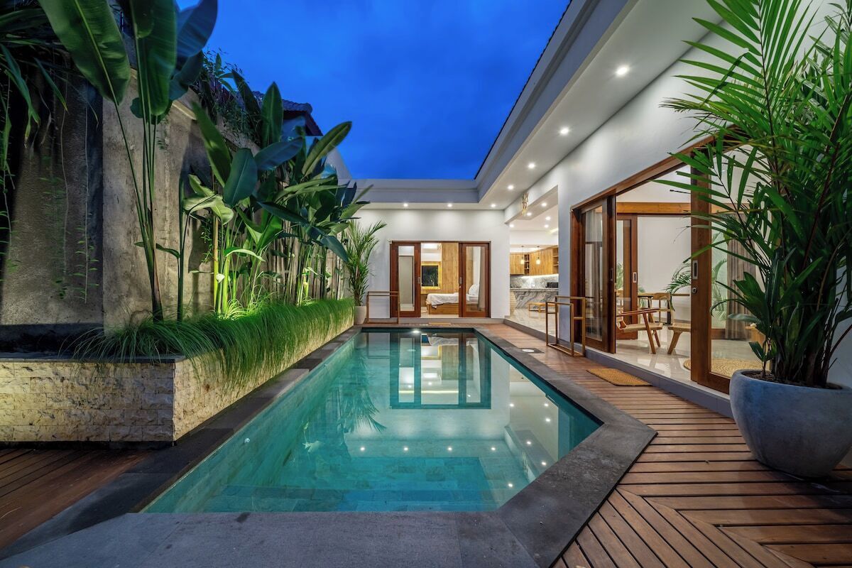 A modern pool area with a clear pool, wooden deck, and surrounding greenery.