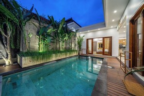 Ein moderner Poolbereich mit klarem Pool, Holzterrasse und tropischen Pflanzen.