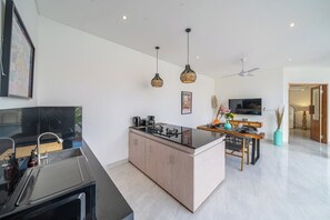 Une cuisine moderne avec un îlot central, un coin repas avec une table et des chaises, et un téléviseur en arrière-plan.