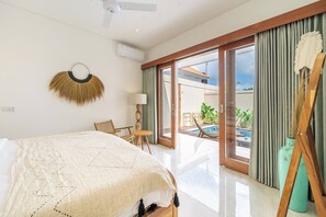 Ein Hotelzimmer mit Bett, Deckenventilator, Blick auf einen Swimmingpool und einer Schiebetür zu einem Außenbereich.