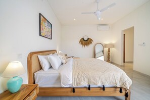 Ein Schlafzimmer mit einem hölzernen Bett, weißer Bettwäsche, einem Wandbild, einem Deckenventilator und einer Nachttischlampe.