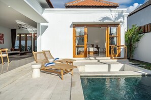 Zona de piscina amb gandules i taula petita, un porxo cobert amb vista a la piscina i una porta corredissa de vidre que dona a un espai interior.