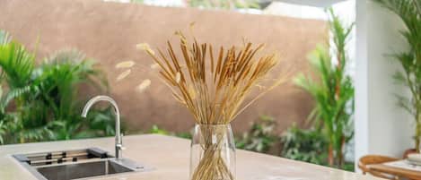 Una cocina de diseño moderno, con un lavamanos, un jarrón con espigas de trigo y un cuenco de madera sobre la encimera.
