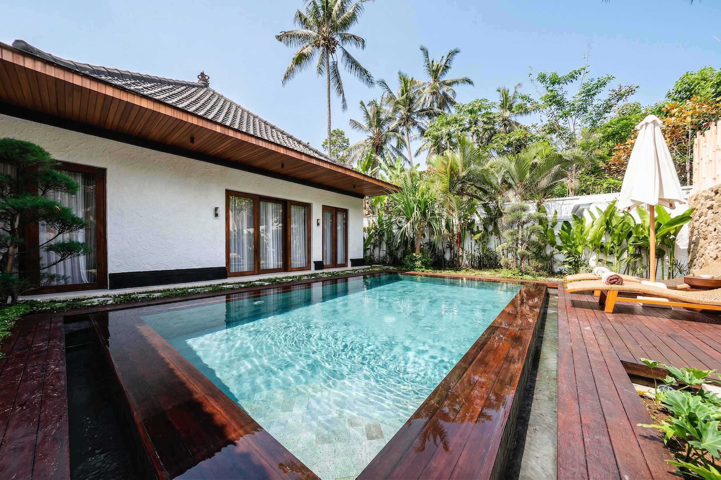 A rectangular swimming pool with clear water, surrounded by a wooden deck and a white building with large windows.