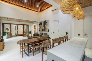 A spacious living area with a wooden ceiling, a dining table with chairs, and a large window. - Tropical 3BR Gem w Huge Pool+Prime Ubud Location (Gianyar Regency)