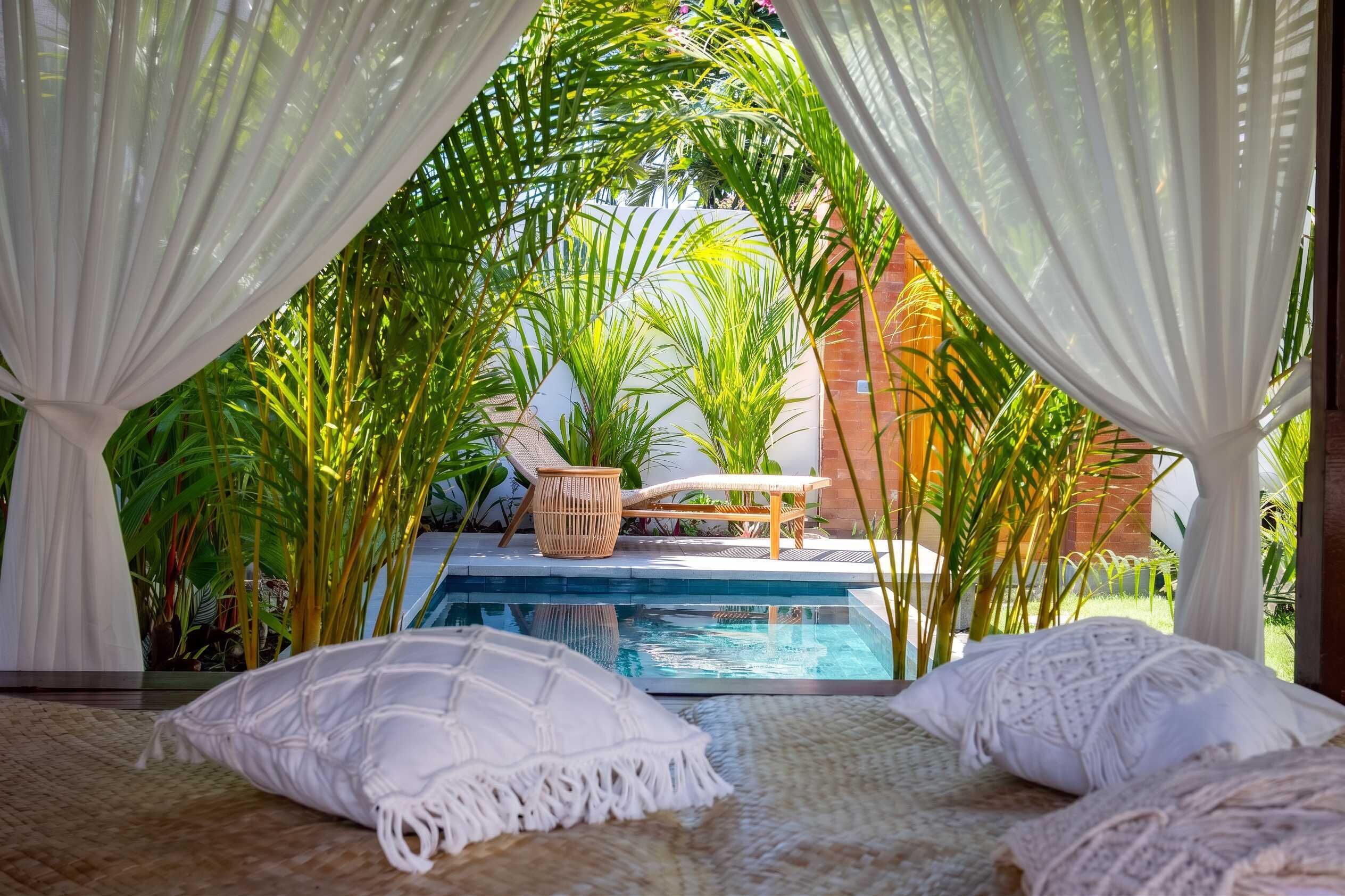 A private pool area with a lounge chair and a small table, surrounded by lush greenery and white drapes.