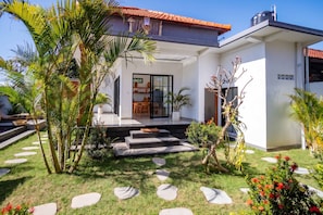 Ein modernes Haus mit Terrasse, Essbereich und Garten mit Palmen und trittfesten Steinen.