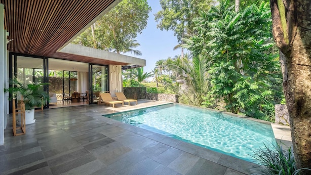 Ein moderner Poolbereich im Freien mit einer Steinterrasse, Liegestühlen und einer Holzpergola.