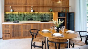 Eine moderne Küche mit Holzschränken, einer grunen Fliesenspiegel und einem Essbereich mit rundem Tisch und Stühlen.