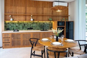 Eine moderne Küche mit Holzschränken, einer grunen Fliesenspiegel und einem Essbereich mit rundem Tisch und Stühlen.