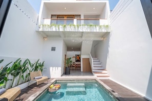 Ein modernes, zweistöckiges Haus mit Swimmingpool, Gartenmöbeln und einer Treppe, die zum oberen Stockwerk führt.