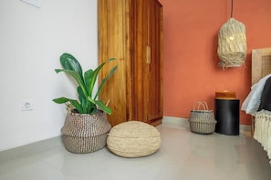 Habitació amb un armari de fusta, una planta en test, un petó teixit, una cistella de vímet i una làmpada penjant.