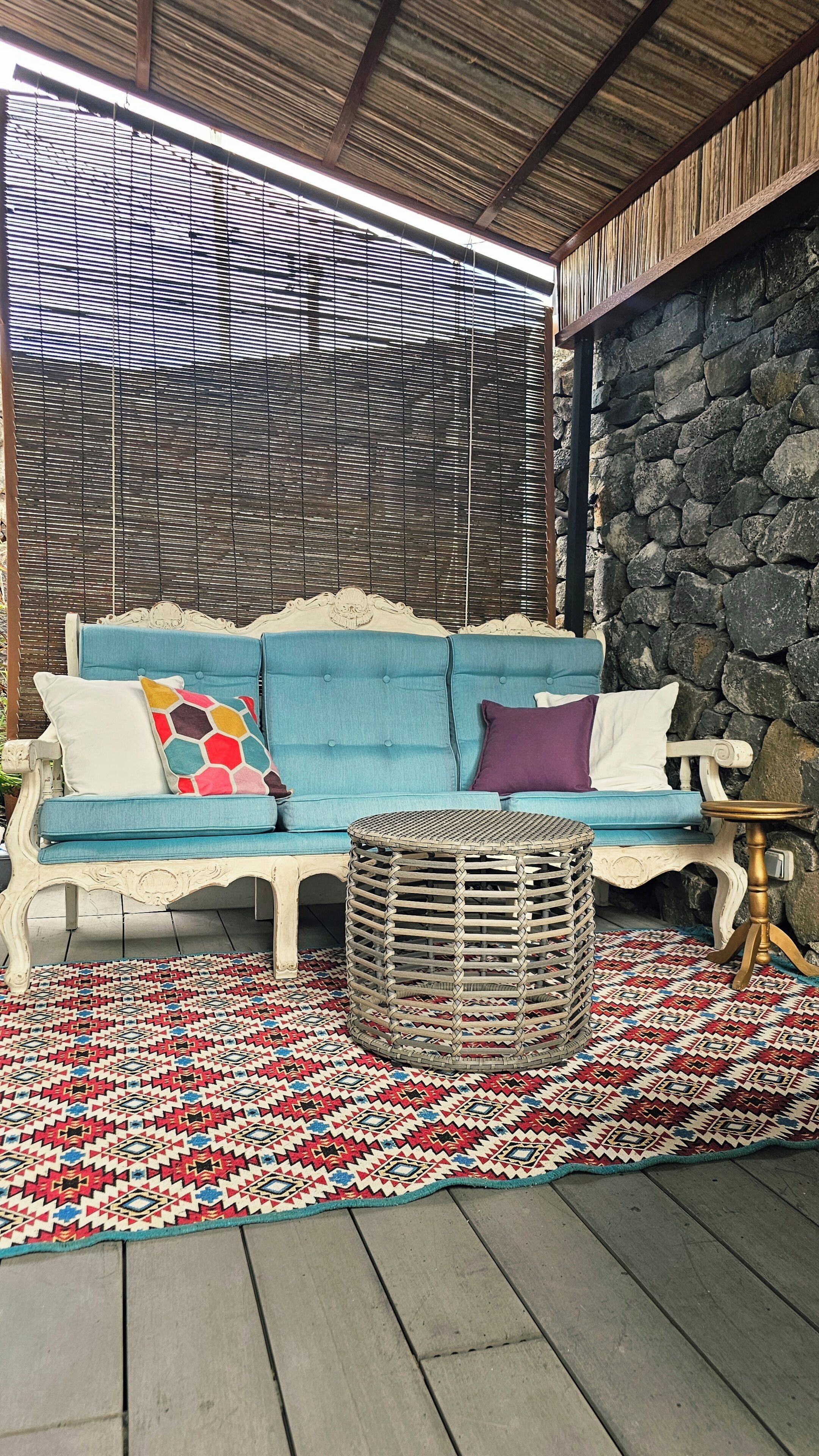 Un divano blu con cuscini decorati, un cesto intrecciato e un tappeto a motivi su un pavimento di legno.