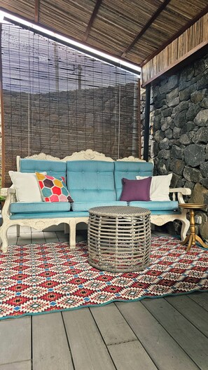 Un canapé bleu agrémenté de coussins à motifs, un panier en osier et un tapis à motifs posés sur une terrasse en bois.