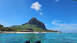 A tropical beach with clear turquoise water, a prominent mountain, and a small boat. - The loft - A charming hideaway heaven (Rivière Noire)