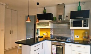 Een keuken met een zwart aanrecht, witte kasten, een roestvrijstalen afzuigkap, een magnetron en hanglampen.