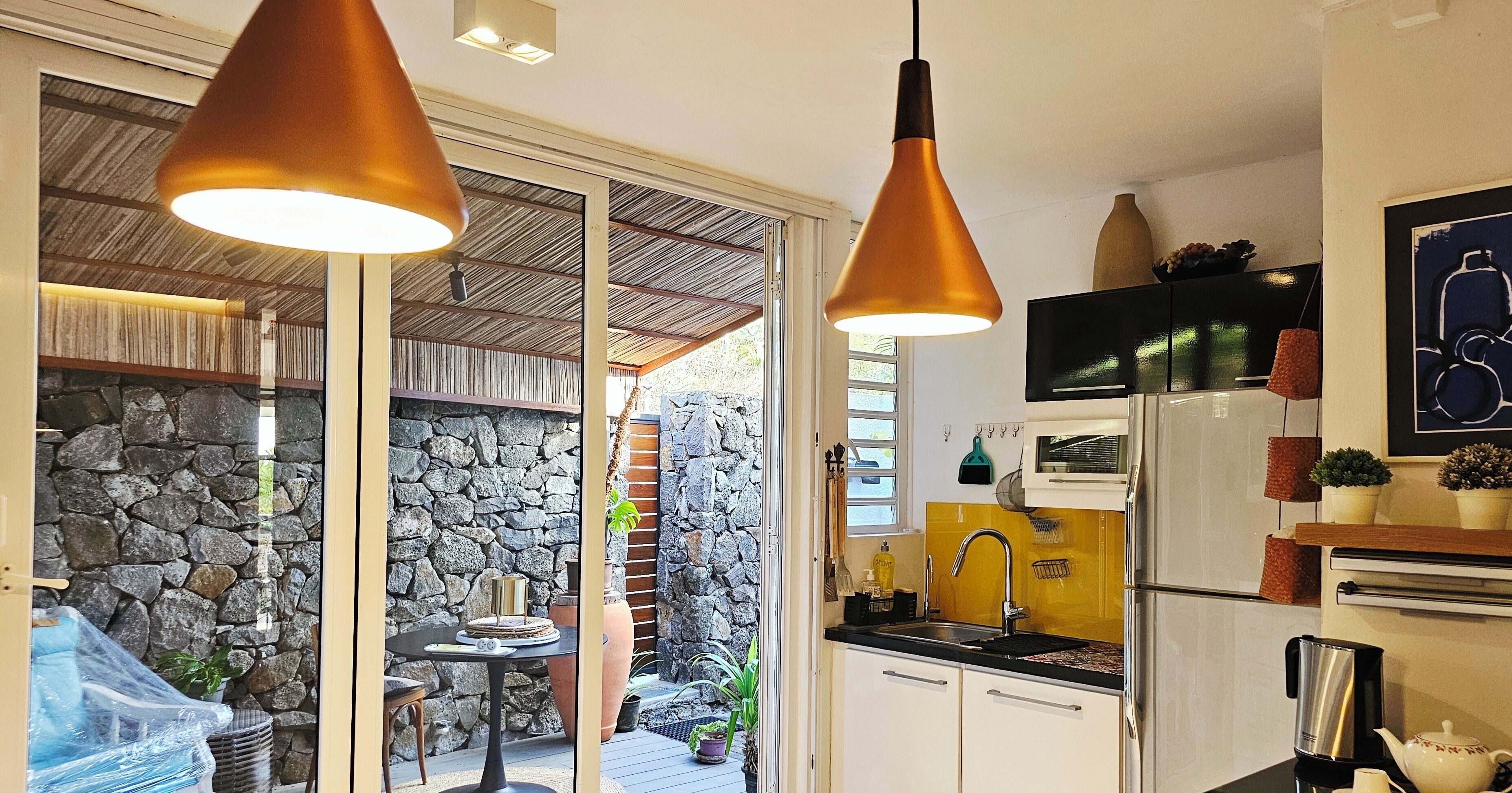 A modern kitchen with a stone wall, a dining area with a table and chairs, and pendant lighting.