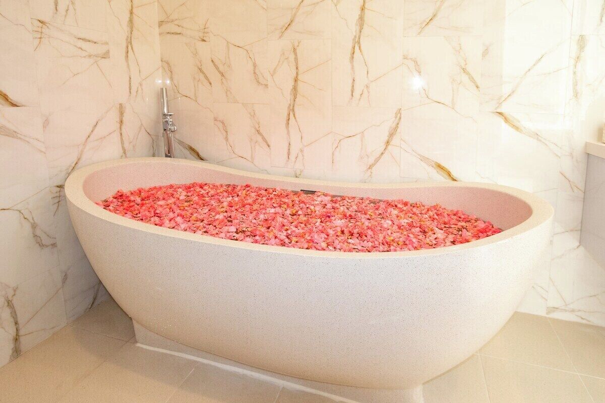 Une baignoire sur pied remplie de sels de bain roses, placée devant un mur de marbre.