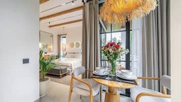 Een moderne hotelkamer met een eethoek, een groot raam met gordijnen en een hanglamp.