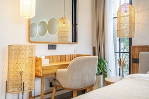 Une chambre d’hôtel avec un bureau en bois, une chaise, un lit, un grand miroir et deux luminaires suspendus.