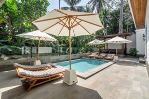 A poolside area with lounge chairs and umbrellas, surrounded by lush greenery. - New Cozy 1BR • Jungle View • Pool&Garden • Balcony (Kabupaten Gianyar)