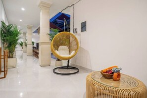 Un interior modern amb una cadira penjant, una taula de vimetla i plantes en testos.