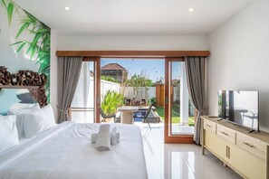 Ein Hotelzimmer mit einem Bett, einem Fernseher, einem Balkon mit Gartenblick und einem Essbereich.