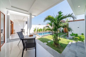 Un pati exterior modern amb piscina, envoltat d'un jardí ben cuidat i una paret blanca.