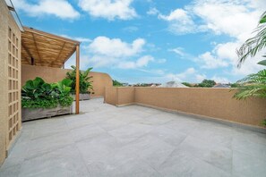 Eine Dachterrasse mit einer Pergola, Blumentöpfen und Blick auf die Stadtlandschaft.