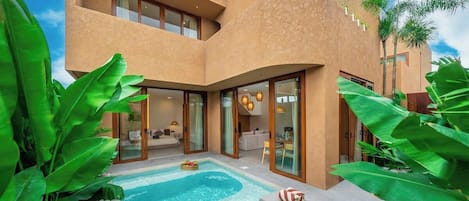 A modern building with a swimming pool, lounge area, and glass doors leading to an interior space.
