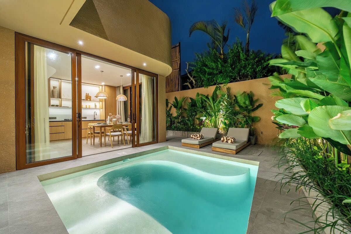 A swimming pool with lounge chairs, a kitchen area, and a dining space visible through glass doors.