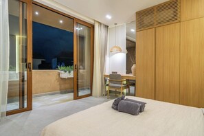 Ein Schlafzimmer mit einem Bett, einem Schreibtisch und einem Sessel. Eine Glastür führt zu einem Außenbereich.