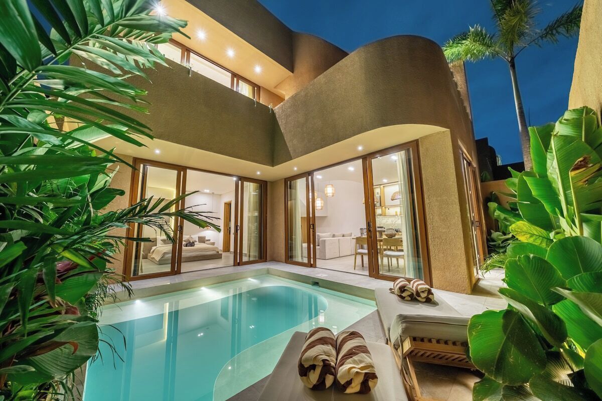 A modern poolside area with a clear pool, lounge chairs, and a glass-enclosed living area.